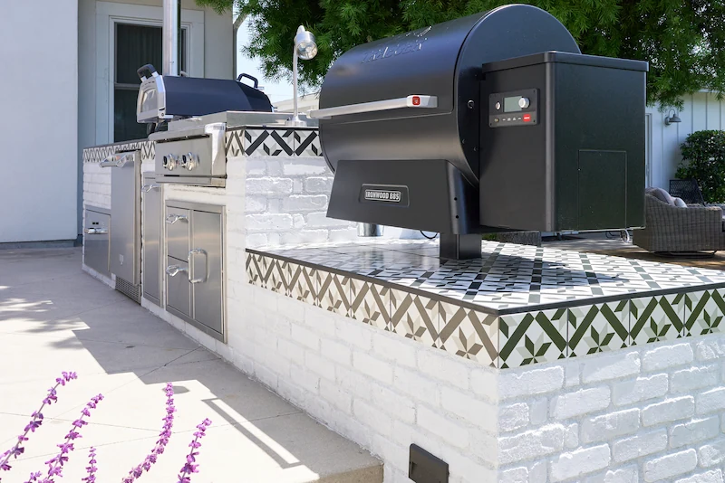 Outdoor grilling station with white brickwork and patterned tile detail, modern black grill, in a sunny patio setting. Photo by Todd Huge.