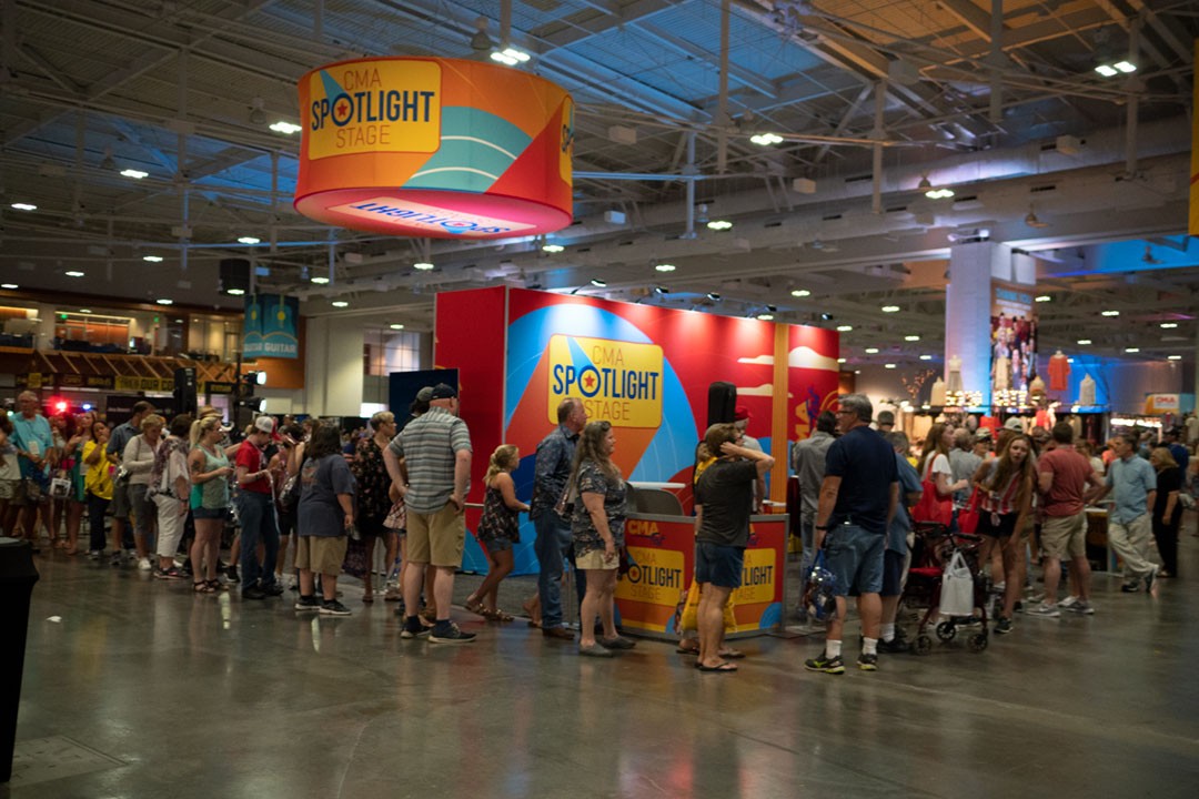 Crowds gather around the CMA Fest Spotlight Stage inside the Nashville convention center, highlighting fan enthusiasm and interactive experiences at the country music festival.