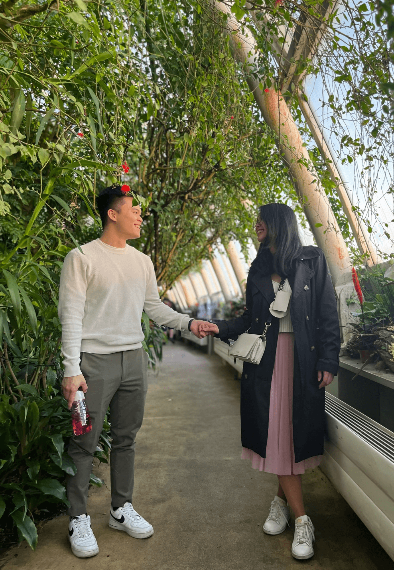 A woman with long blonde hair, in a brown top and jeans, walks through a sunlit forest, holding someone's hand. The scene is warm and inviting.