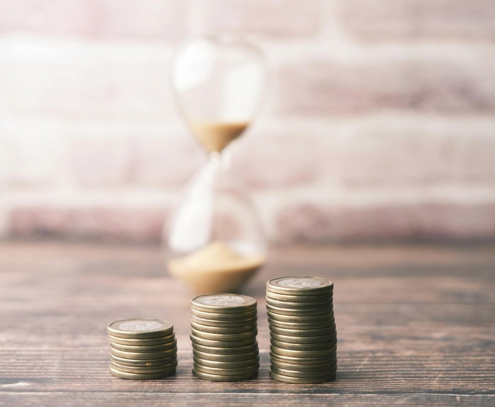 Monedas apiladas junto a un reloj de arena como representación del paso del tiempo en la economía