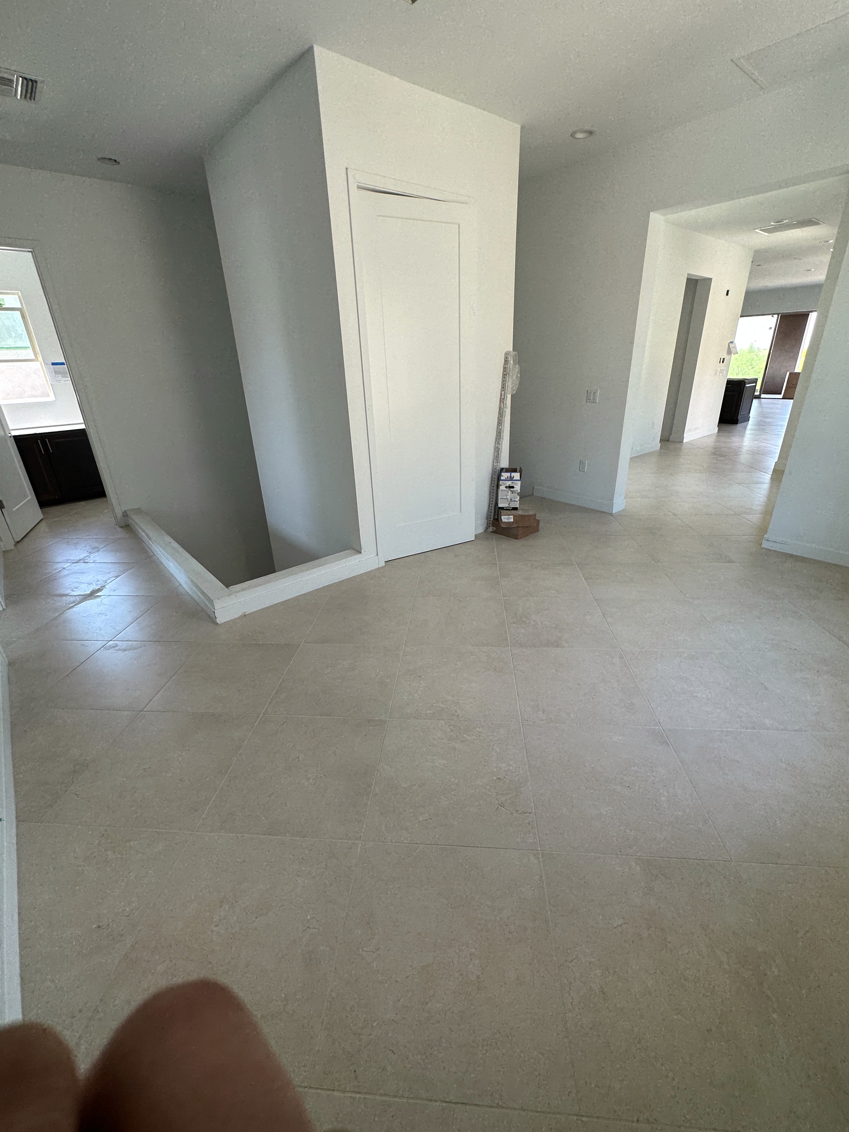 Modern hallway with beige marble tile flooring, staircase, and white walls in a new home under construction.