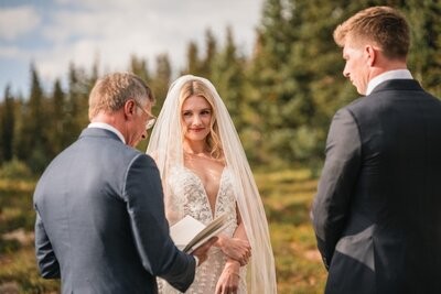 Clemmie smiles toward Tucker while the officiant reads beside them.