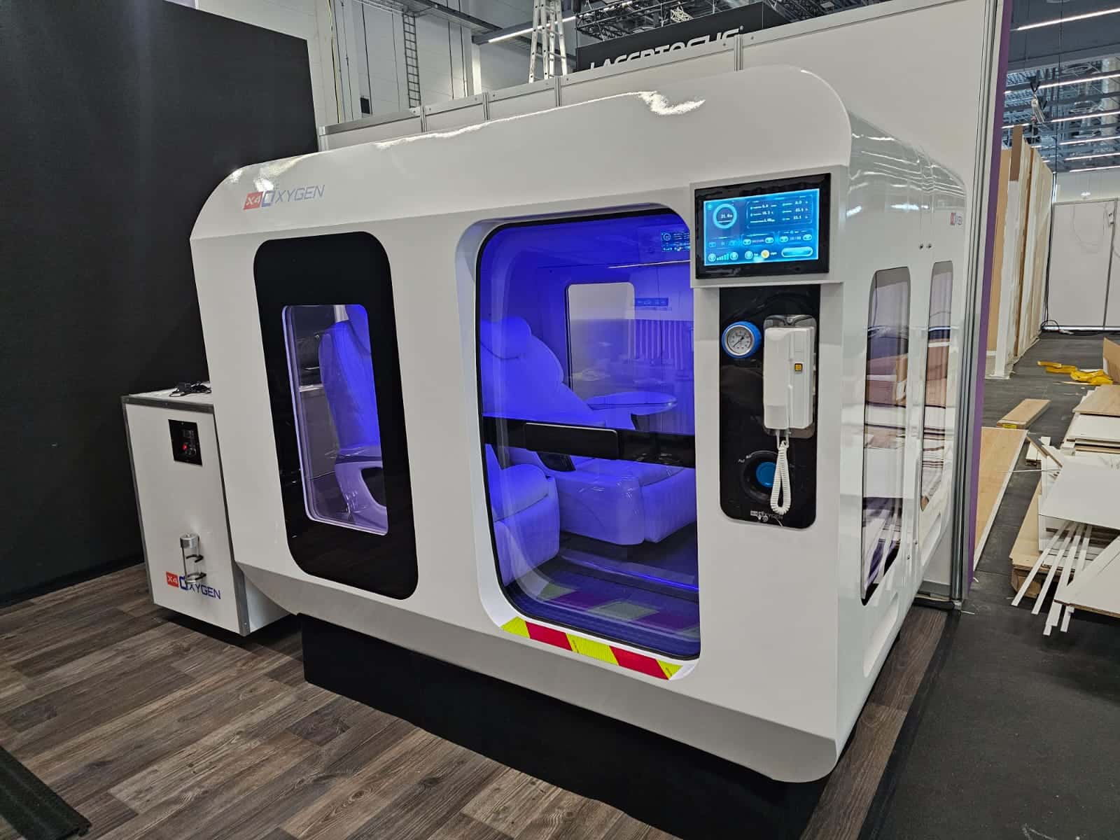 Außenansicht der großflächigen X4OXYGEN X250-20 Druckkabine mit integriertem Überwachungssystem, blauer Effektbeleuchtung und robuster Gehäusestruktur für den Einsatz in Zentren und Kliniken.