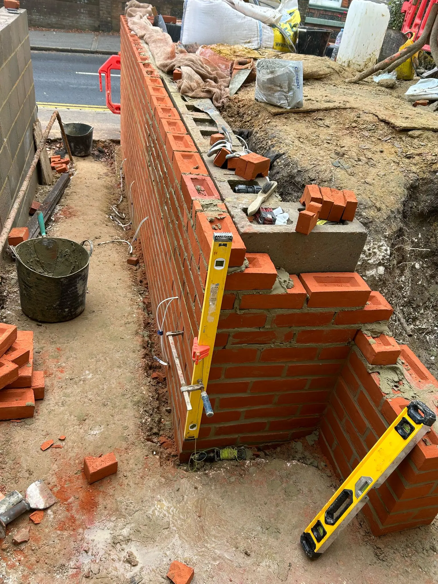 A partially constructed brick wall with a level tool and some bricks scattered on the ground.