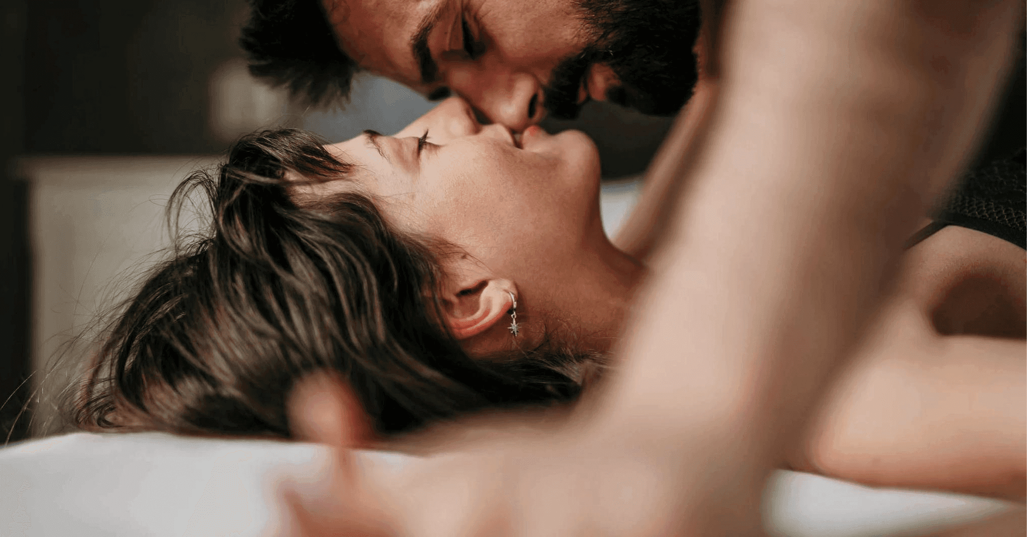 Kvinna ligger i sängen med en man ovanpå henne som är redo att kyssa hennes läppar.