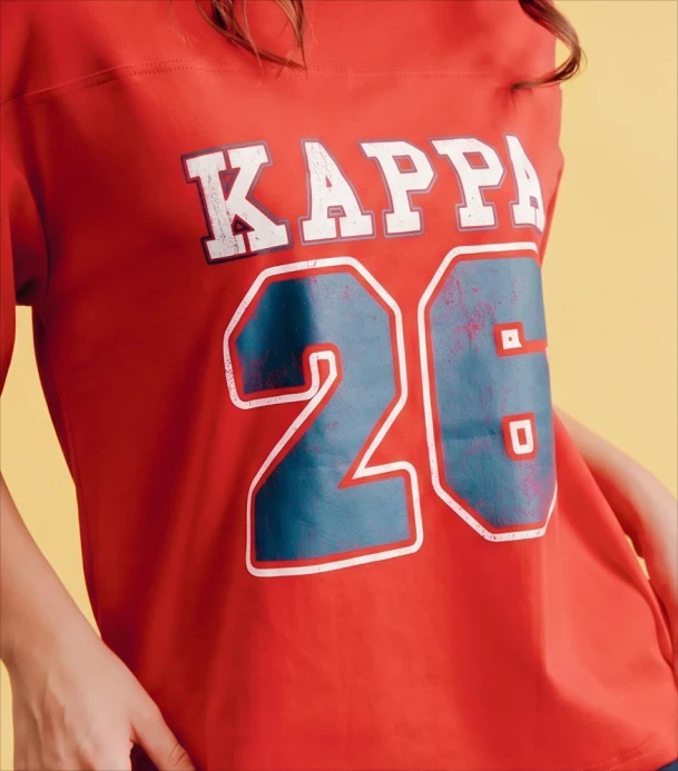Close-up of a person wearing a red jersey tee with distressed white "KAPPA" text and a blue "26" graphic, against a yellow background.