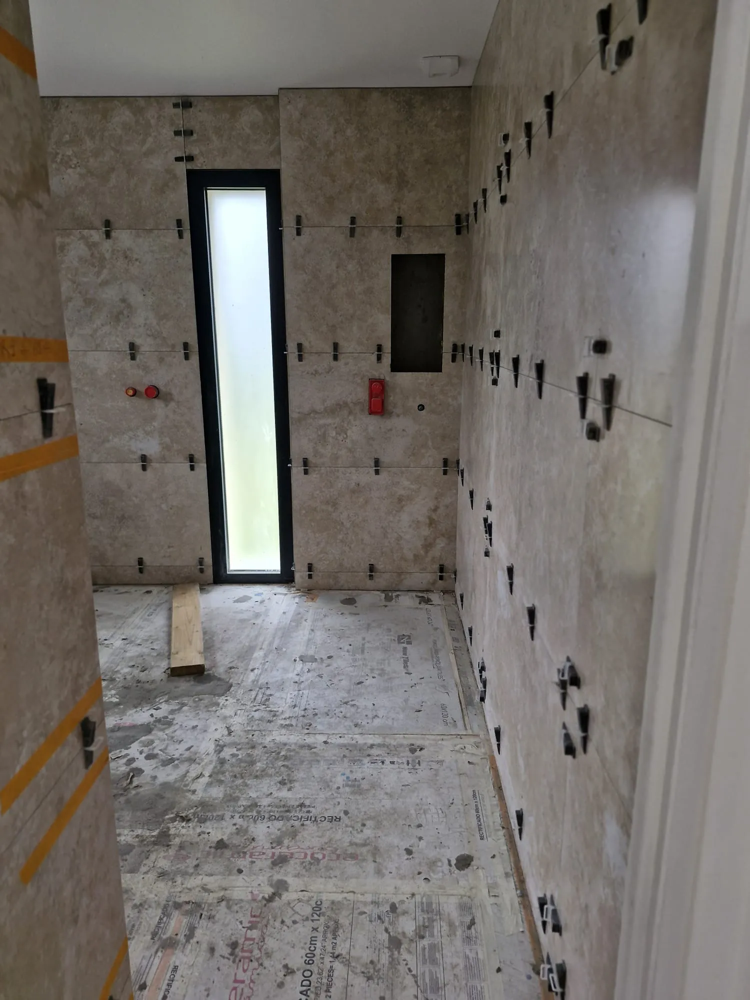 Salle de bain en cours de pose : carrelage mural maintenu par croisillons et cales de nivellement