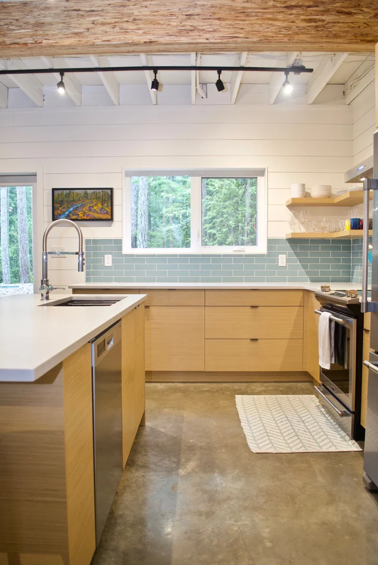 Modern two-story home with large glass windows, warmly lit interiors, and a balcony. Surrounded by trees and a manicured lawn at dusk. Cozy ambiance.