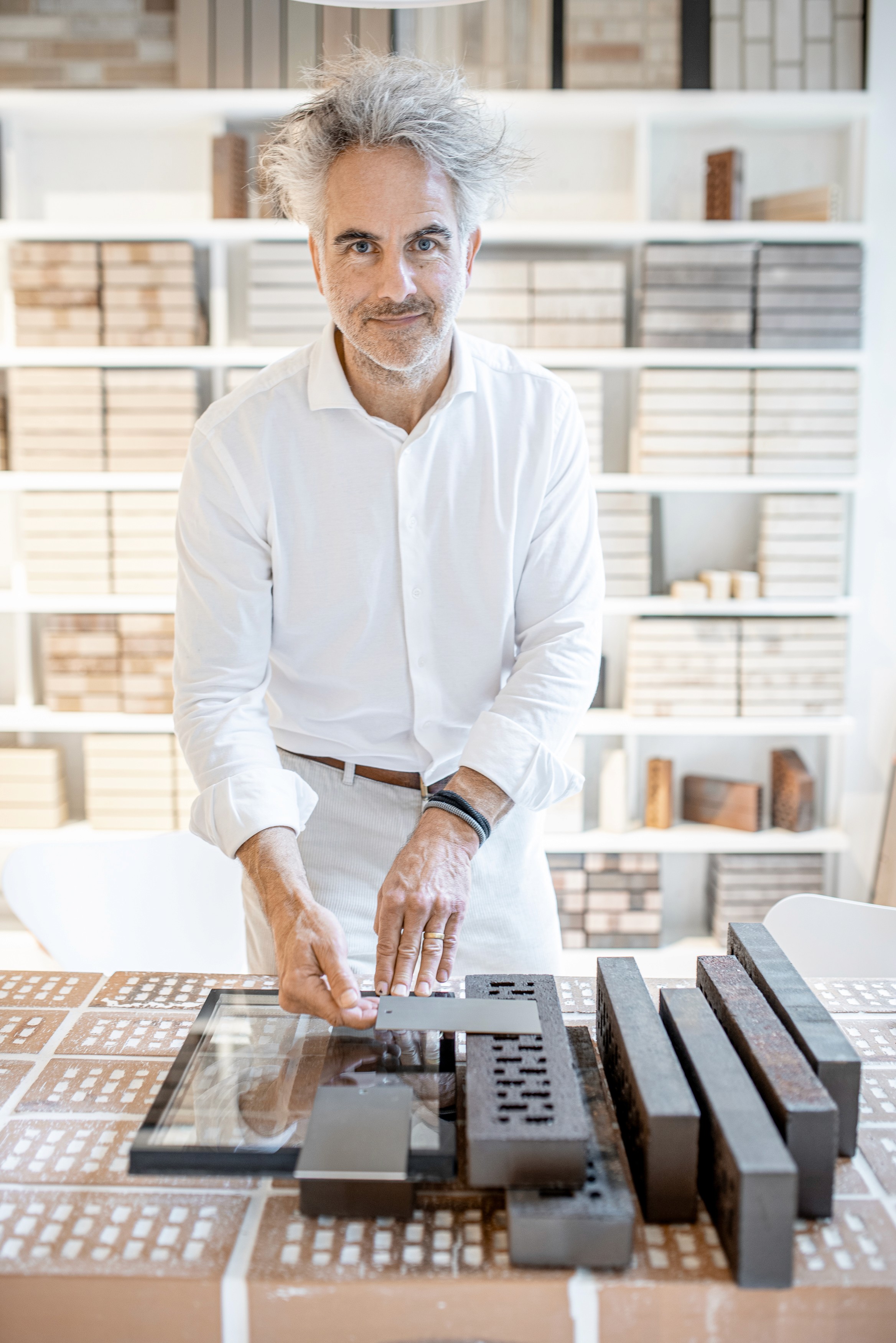 Man onderzoekt baksteenstalen op een tafel met een witte boekenkast erachter.