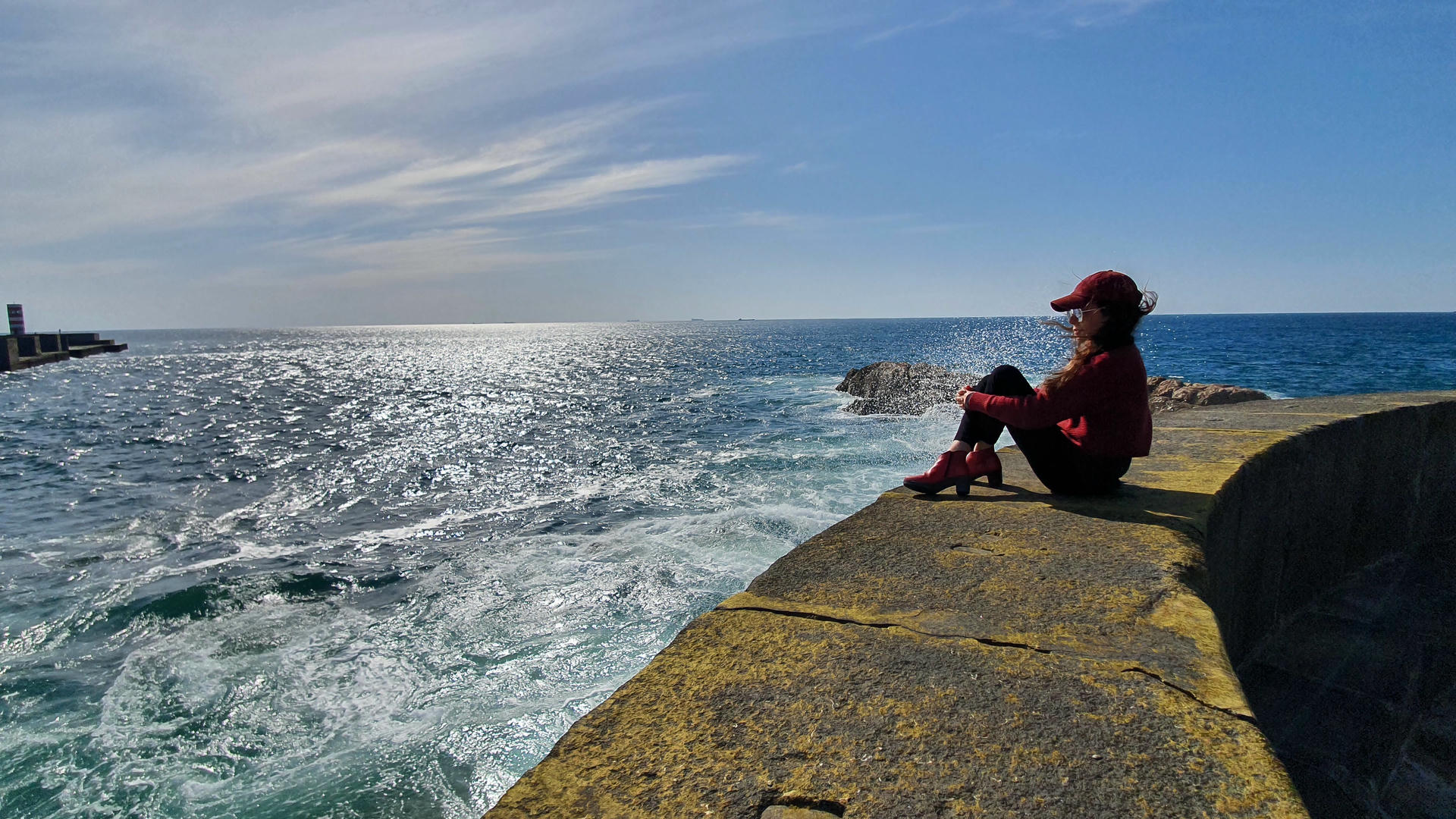 Samira sitting on a wall looking at the ocean