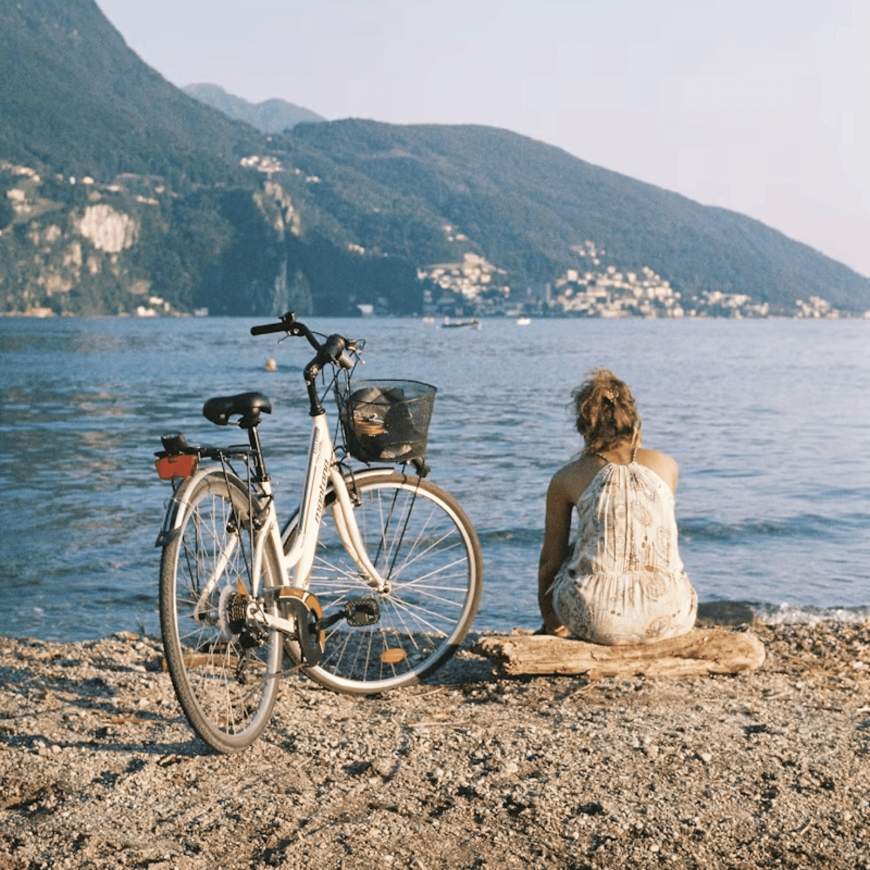 A lady sitting beside her parked bicycle in front of the water