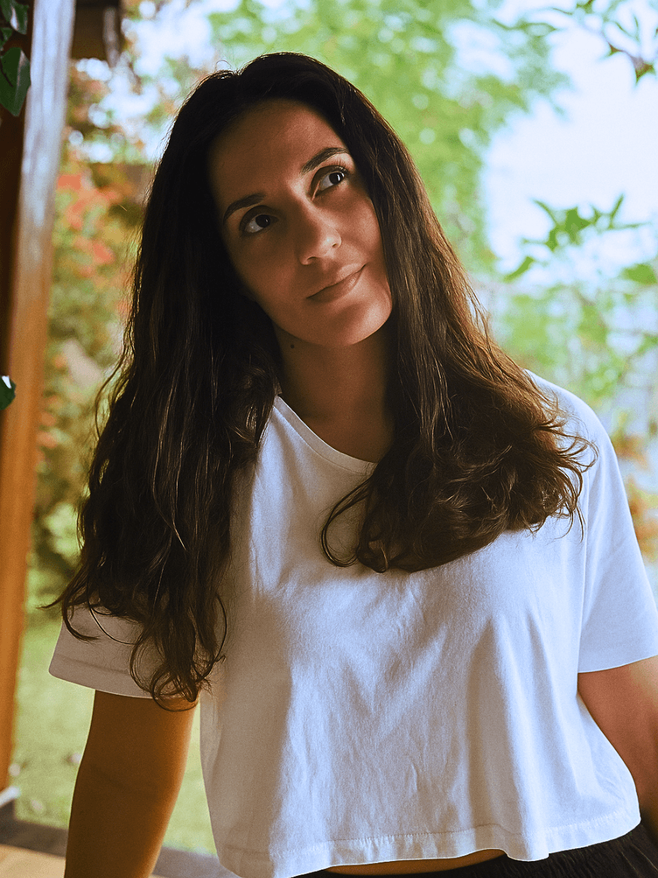 A woman whearing a white loose tshirt is looking up in wonder in front of what seem to be a green garden