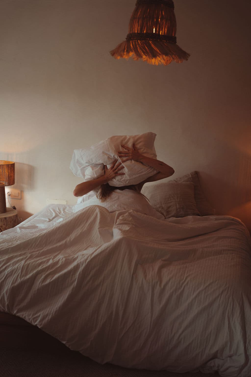 Woman in bed holding a pillow over her face in frustration symbolizing low sex drive in women