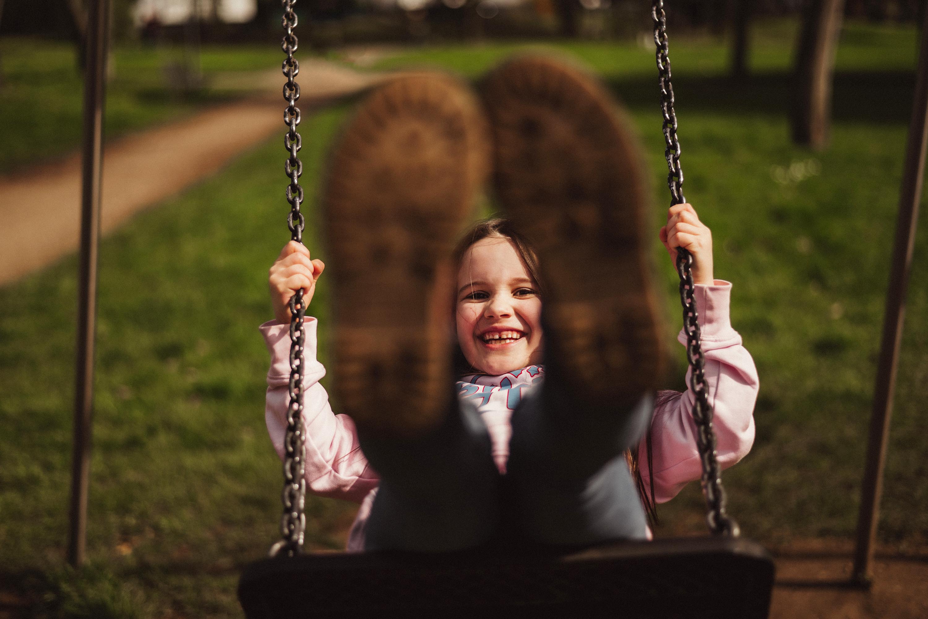 Authentische Kindergartenfotografie Gevelsberg: Ein Mädchen lacht beim Schaukeln glücklich direkt in die Kamera. Professionelles Outdoor-Porträt mit weichem Bokeh-Hintergrund von PK photography 4 Kids NRW.