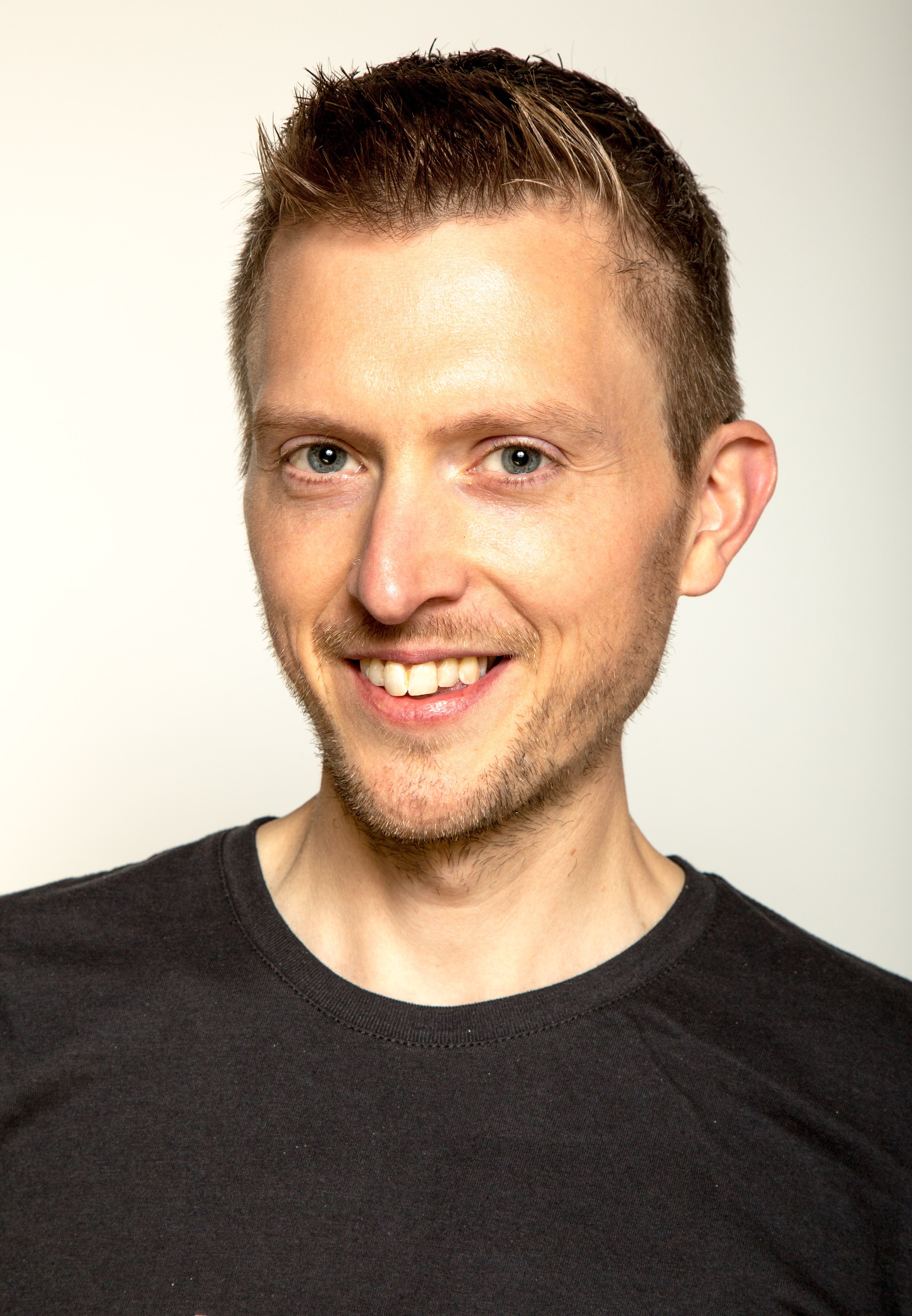 Smiling young man in a black t-shirt against a gray background, radiating warmth and friendliness.