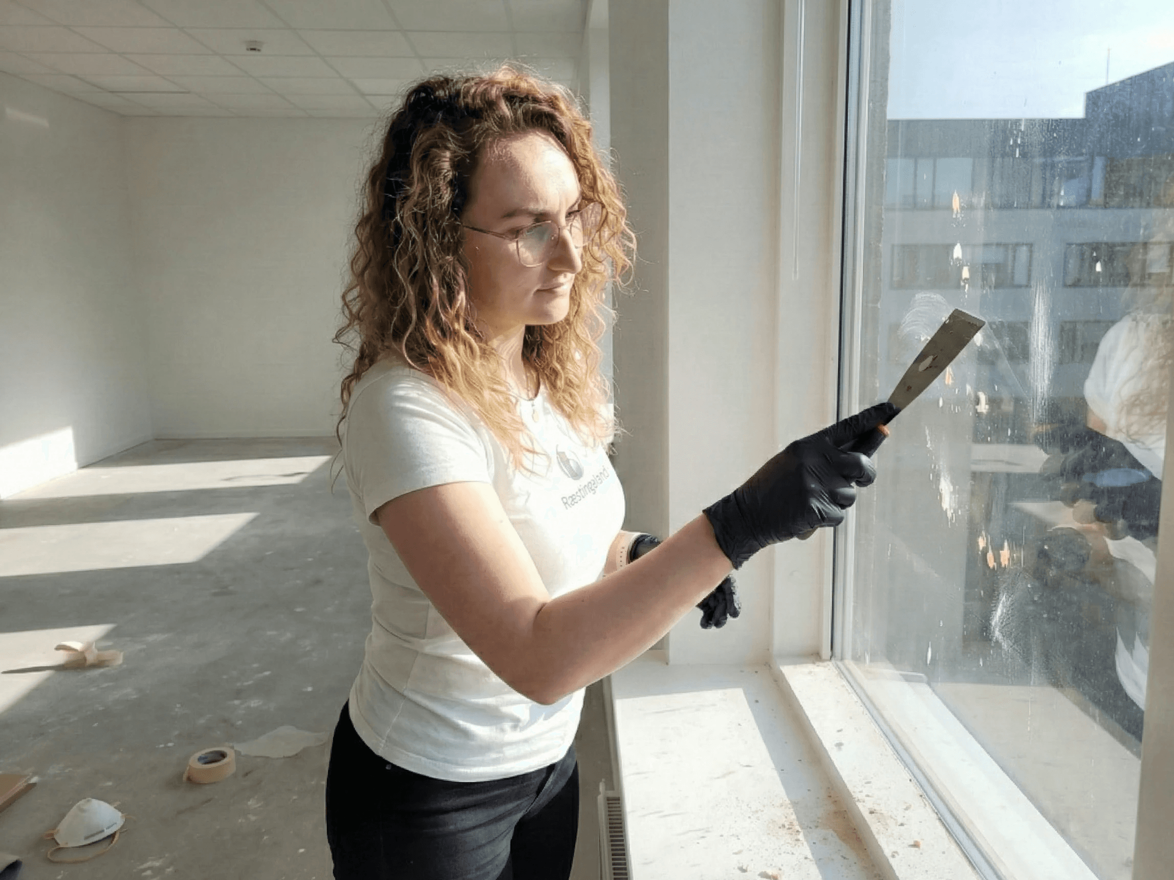 Fjarlæging á óhreinindum af glugga með sköfu.