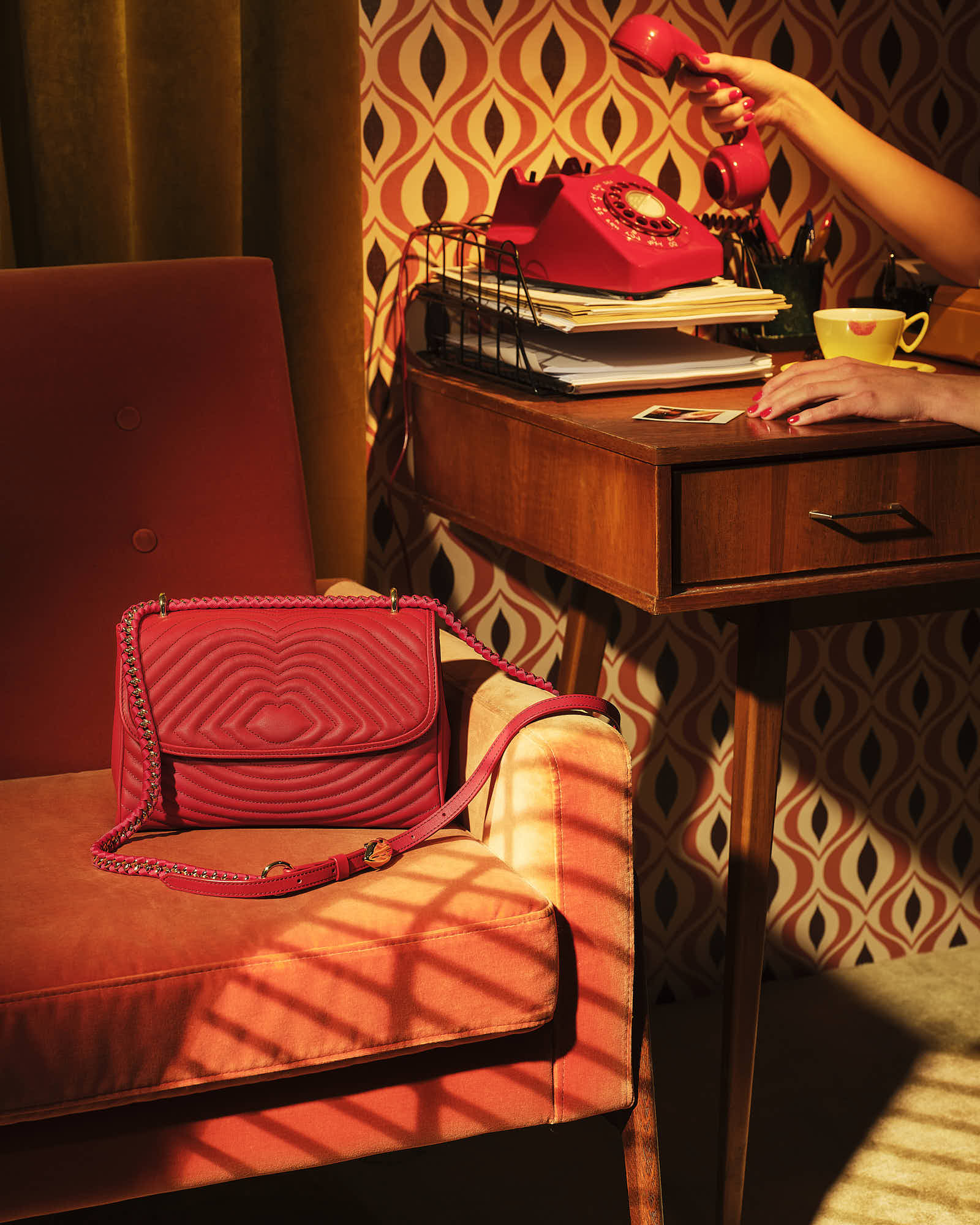 A stylish red handbag rests on a stack of books next to a cozy armchair, creating a warm, inviting atmosphere.