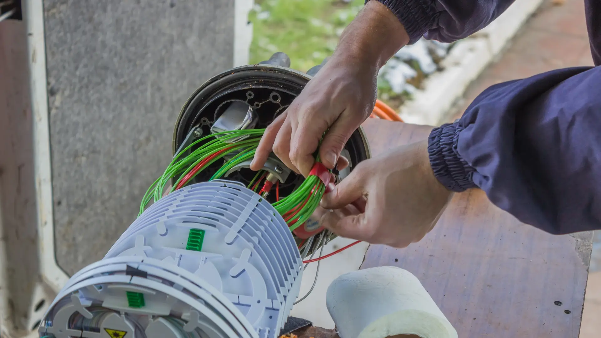 Un technicien fibre optique organise et attache des brins de fibres vertes à l’intérieur d’une boîte de raccordement extérieure.