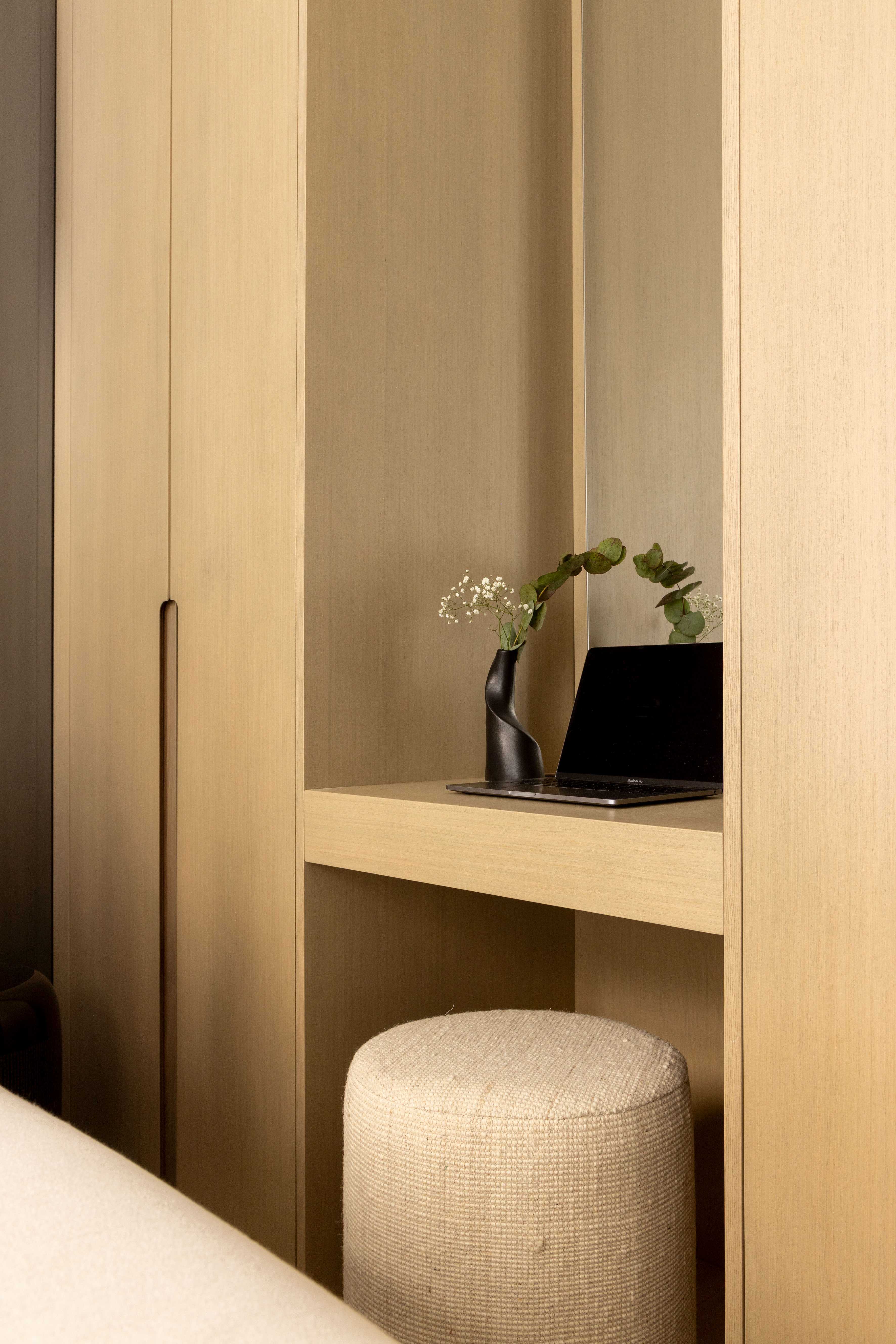 Détail du coin bureau avec laptop, vase noir avec fleurs et pouf en tissu beige
