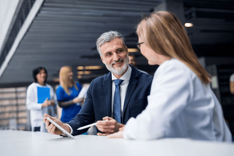 A pharmaceutical sales representative and a doctor talk over a tablet