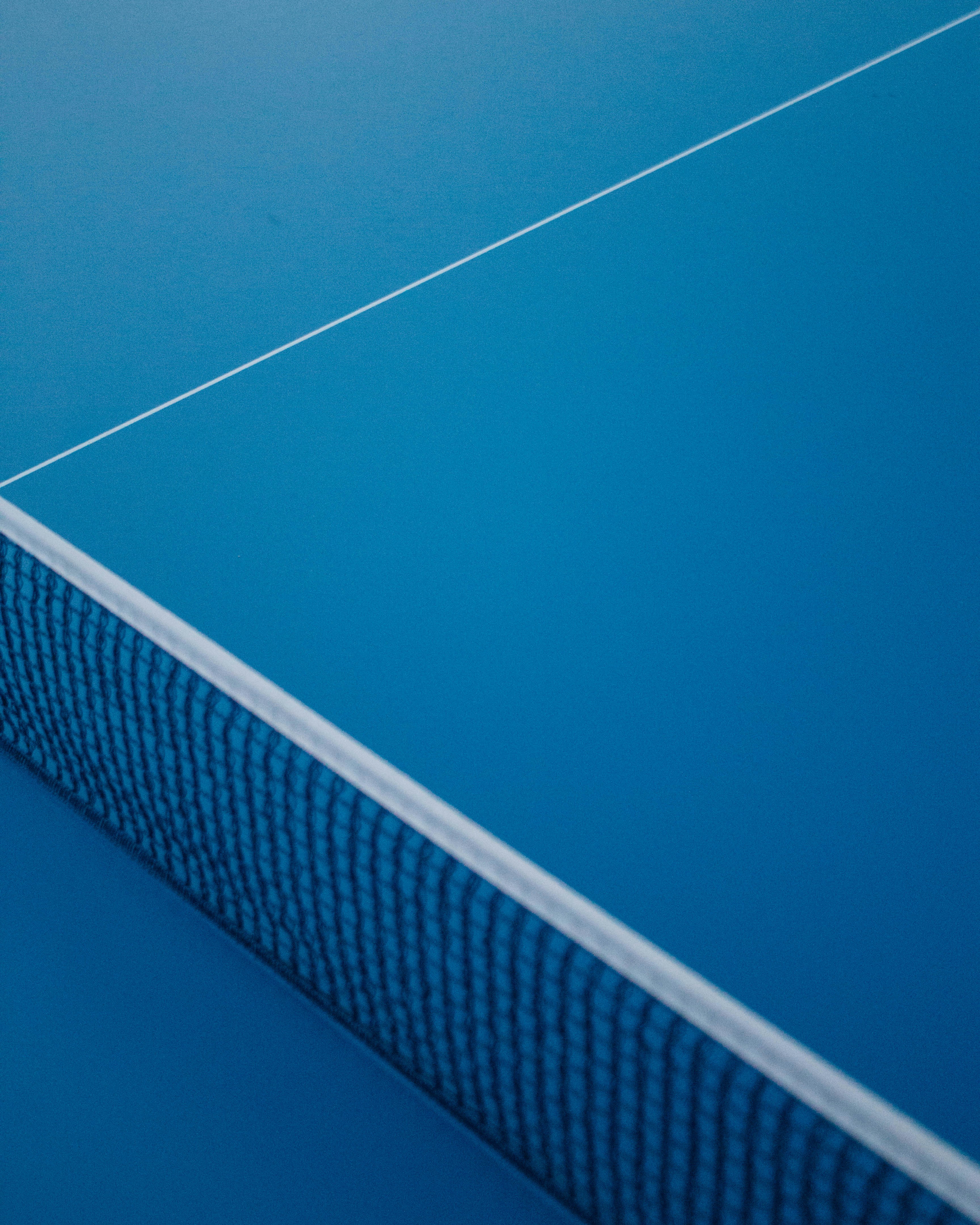 A blue table tennis surface with a close-up view of the white net and boundary line provides a crisp and minimalistic look.