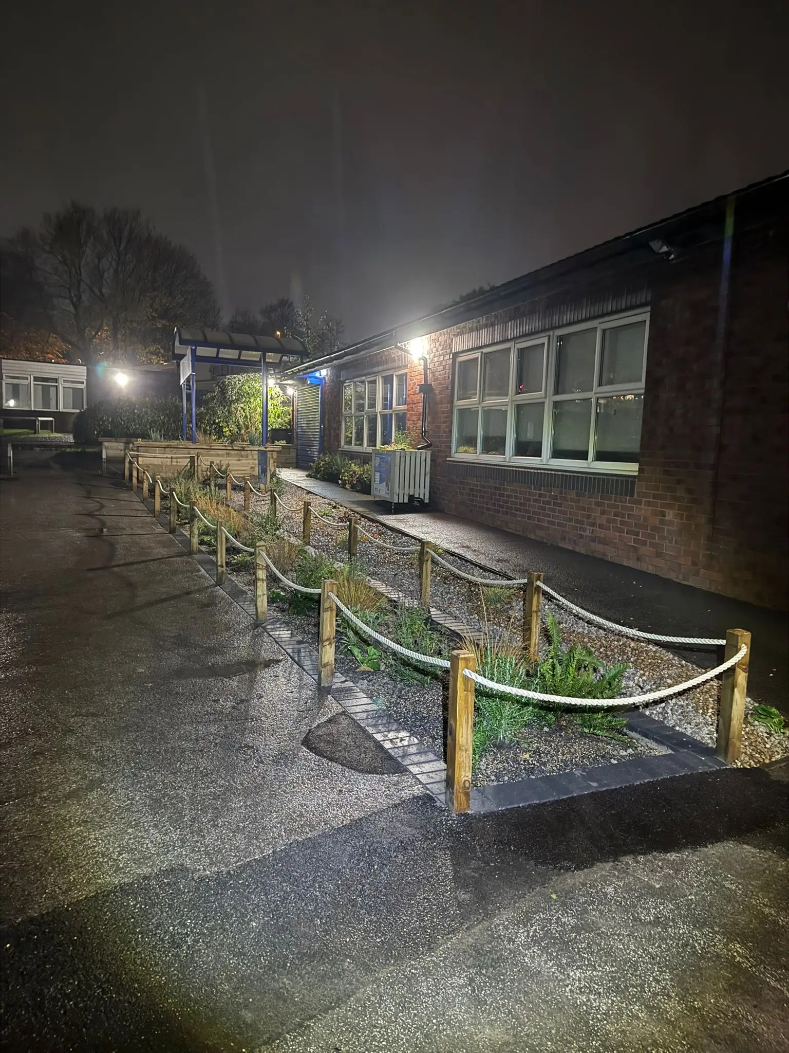 A dimly lit outdoor scene with a long, covered structure and buildings in the background, illuminated by lights.