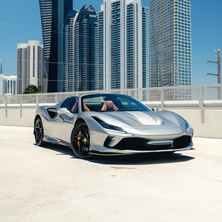 Front 3/4 view of a silver Ferrari F8 Spyder rental in Miami, showcasing its sleek design with a city skyline background.