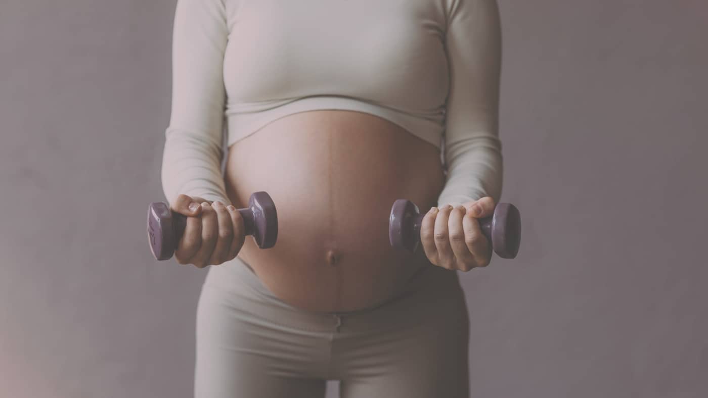 Plan moyen de face sur une femme enceinte en tenue de Pilates claire, effectuant des exercices de bras doux avec de petits haltères de couleur lavande.