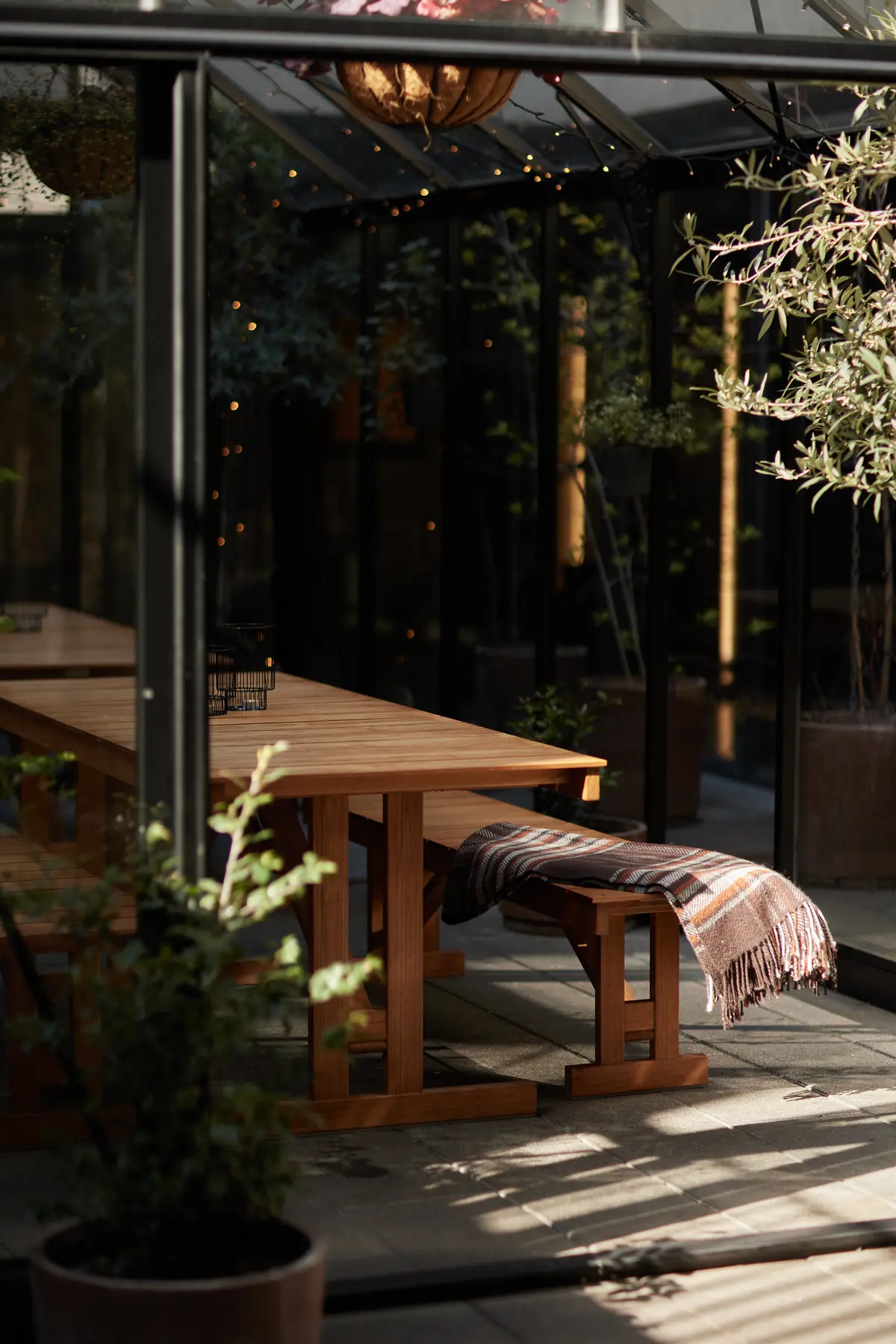 Wooden bench and table with blanket inside the sunlit glass garden house.