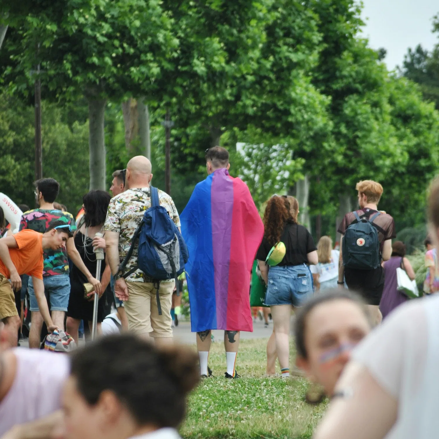 Person draped in bisexual pride flag walking through a park at LGBTQ+ community event in New York City, symbolizing bisexual and pansexual affirming therapy and inclusive mental health support.