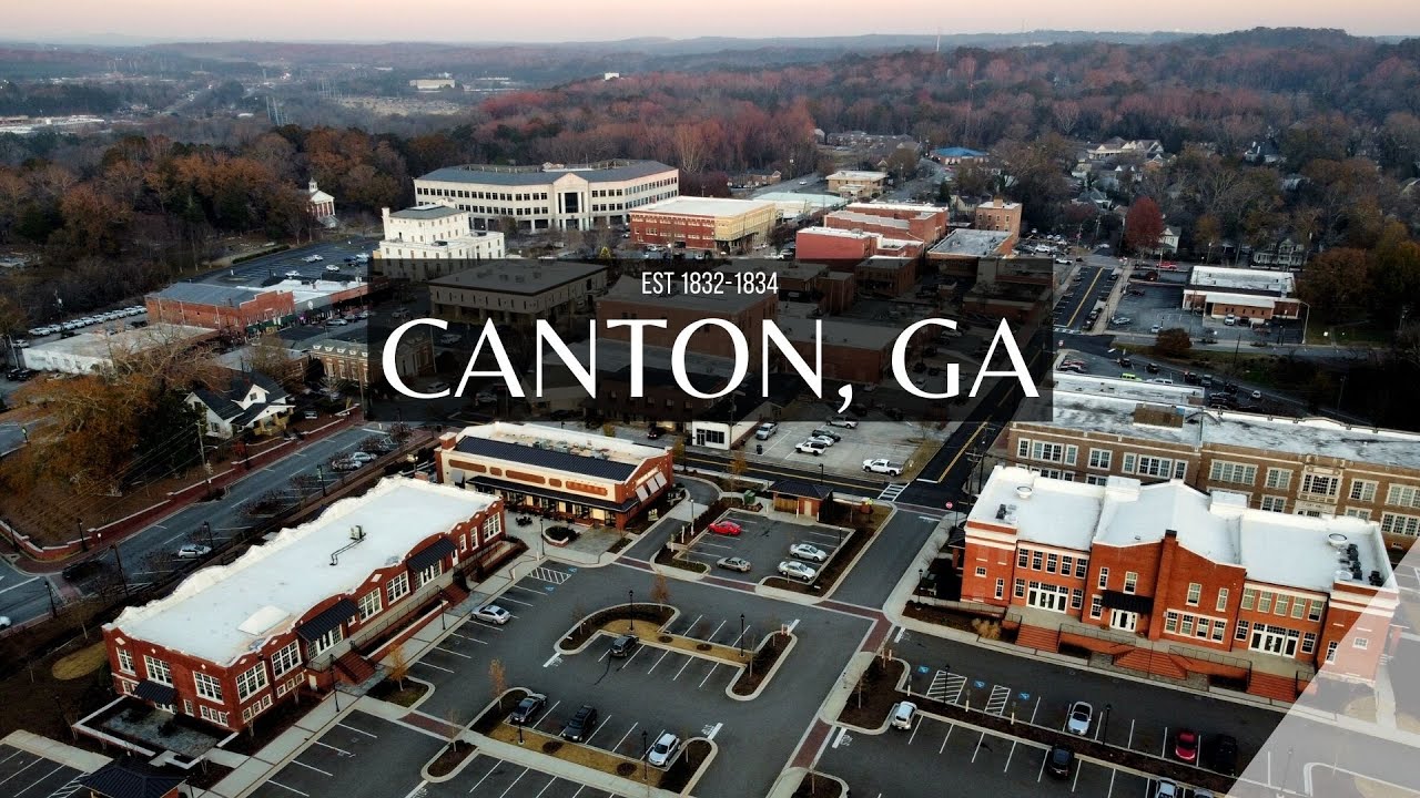 Aerial view of downtown Canton, GA, showcasing historic buildings, parking lots, and tree-lined streets at sunset.