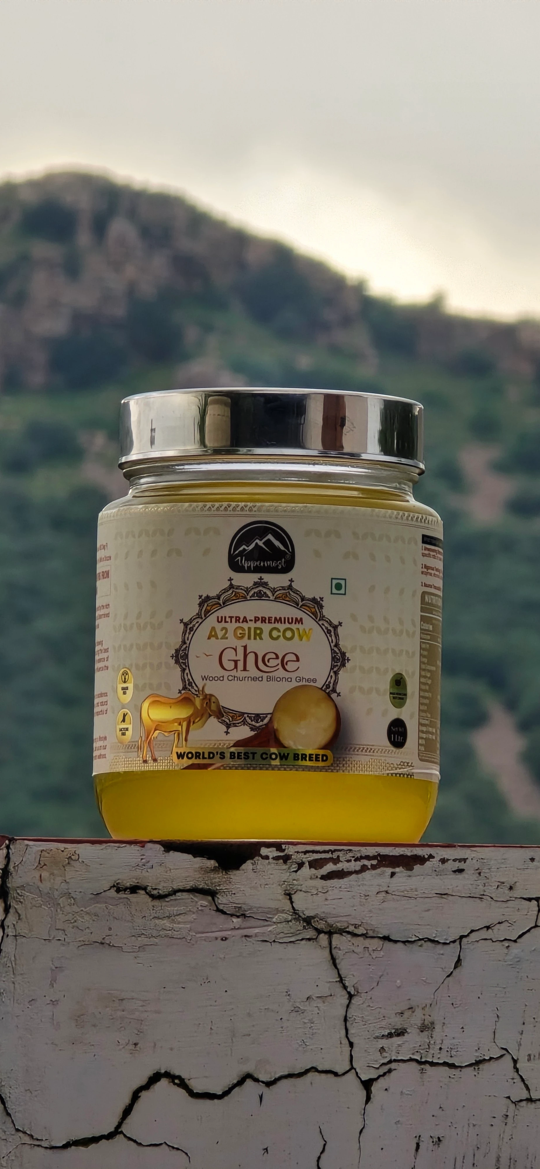 A jar of Uppermost A2 Gir cow ghee against green hills