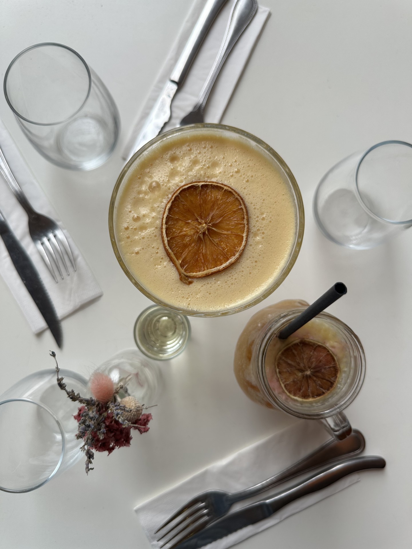 Cozy cafe corner with a round terrazzo table surrounded by wooden chairs, decorated with potted plants and a large mirror reflecting warm light.