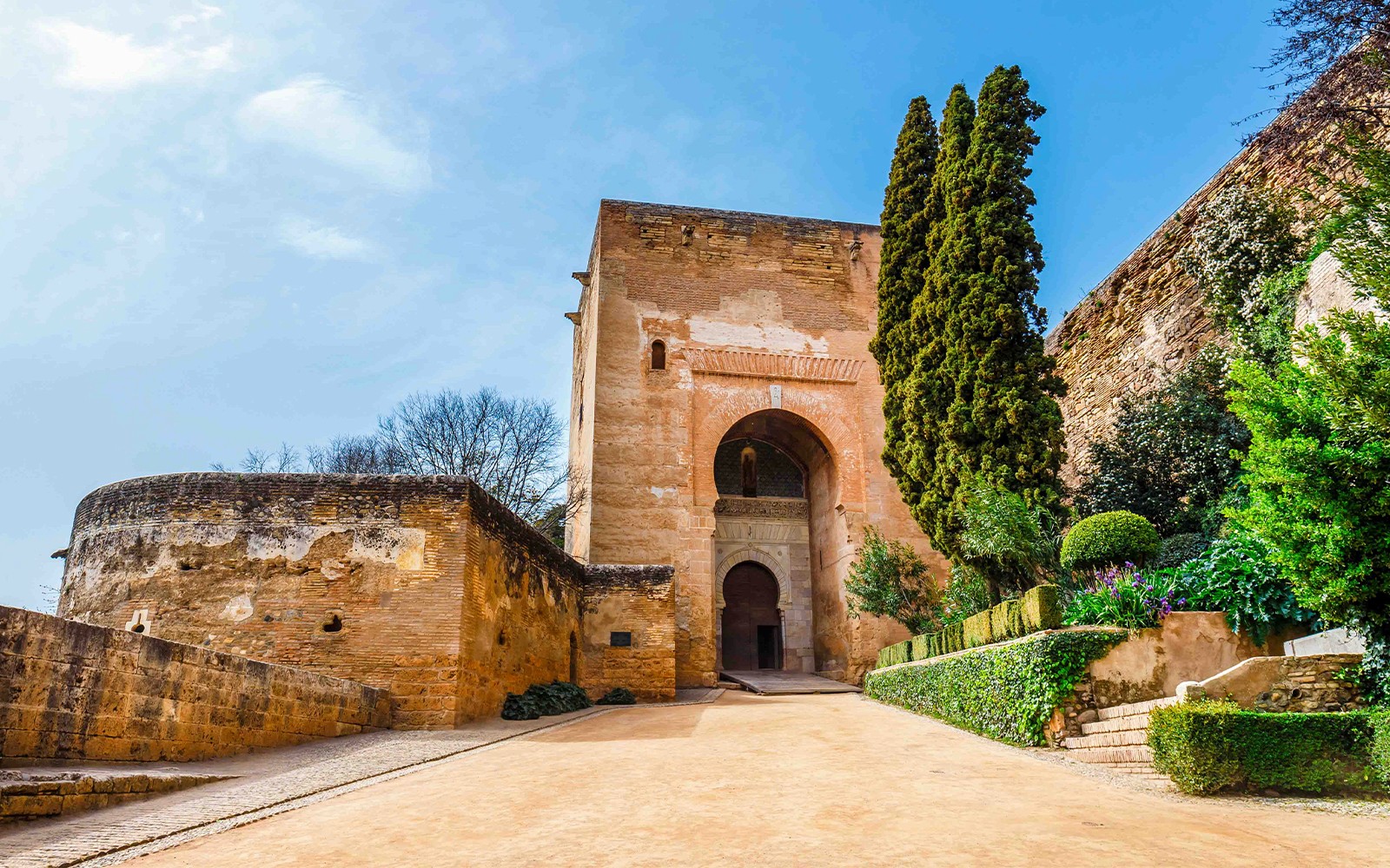 Inngang til Alhambra med steinvegger og frodig grøntområde, Granada, Spania.