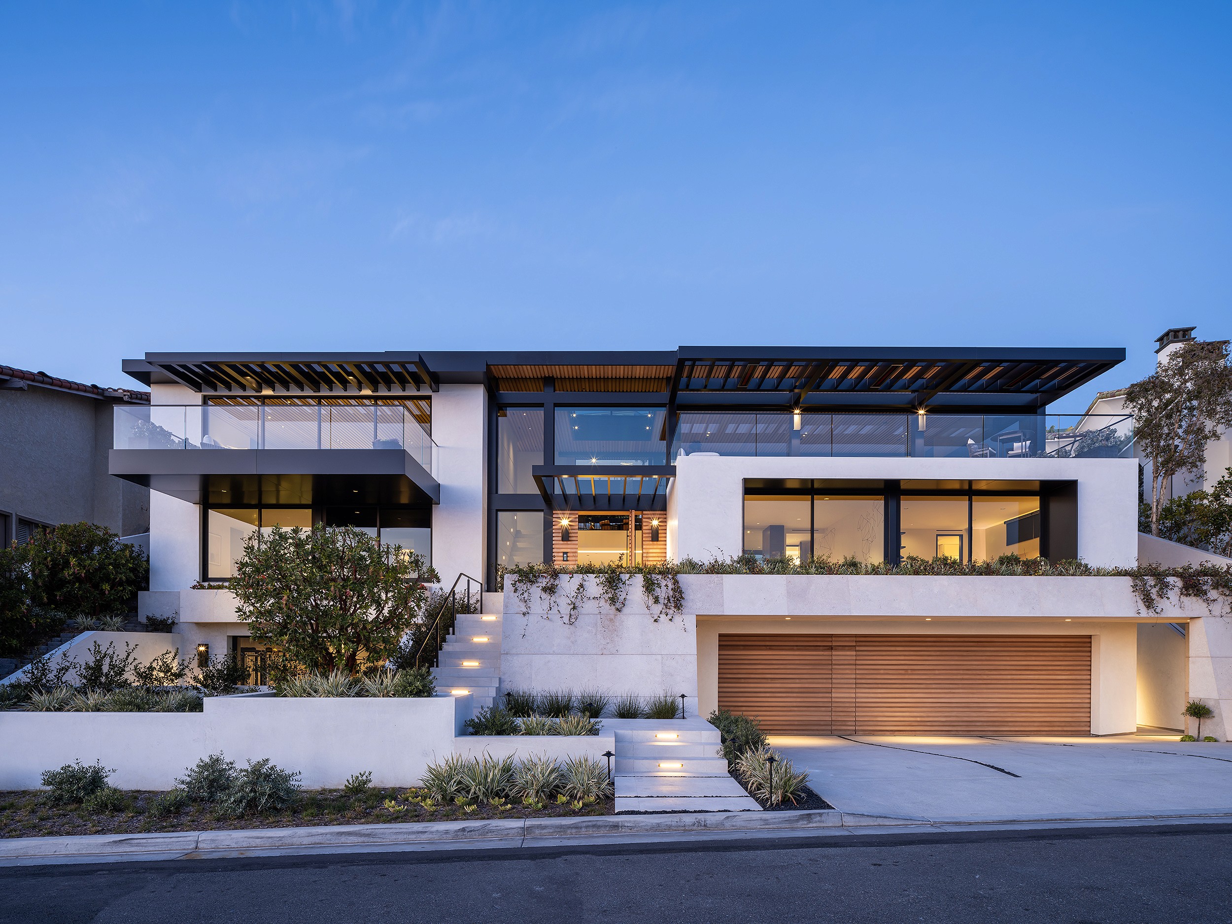 A modern custom home in Newport Beach with contemporary architecture with large glass windows and a wooden garage door.