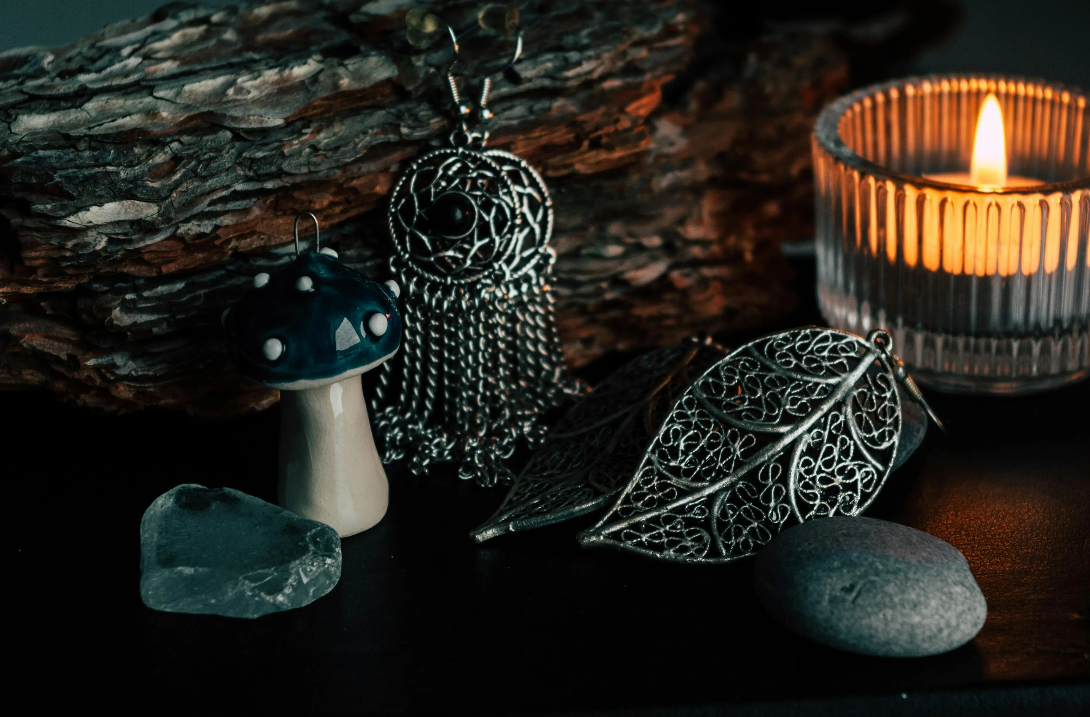 a quartz crystal, a ceramic mushroom, a stone, a candle and some metal pieces on a counter displayed as in a ritual