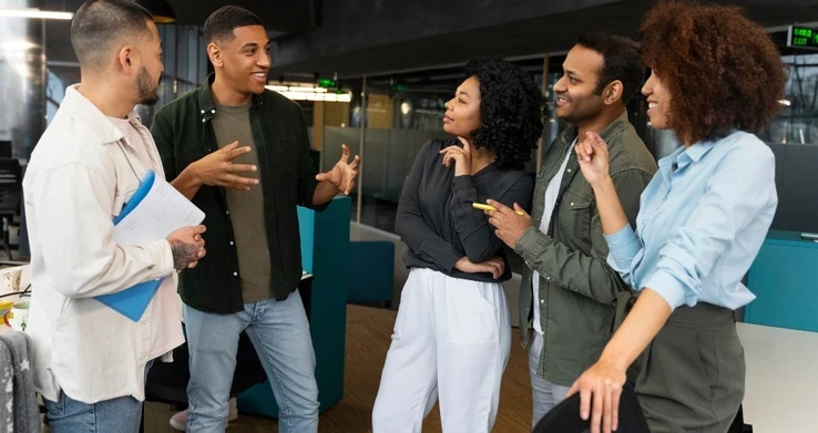 Cinco pessoas de pé conversando em roda num escritório, uma delas gesticulando