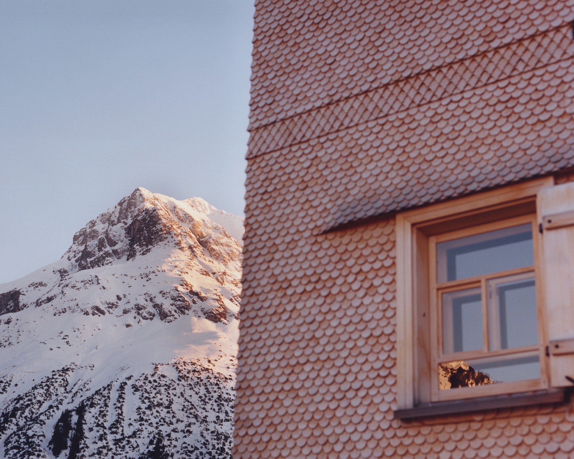 The wooden facade of Chalet Sonnenhof with Omeshorn mountain covered in snow in the background - Lech am Arlberg
