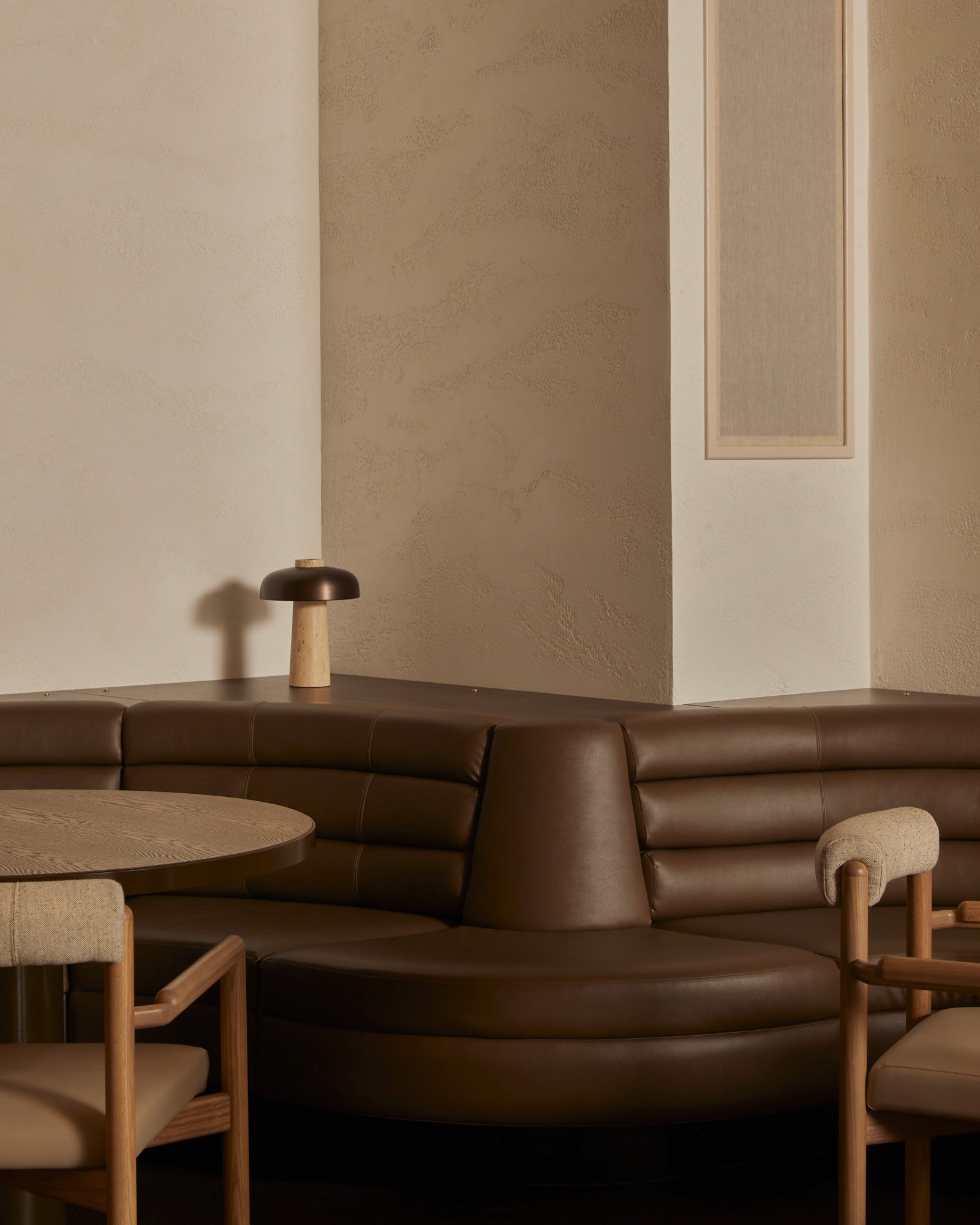 Curved brown leather banquette seating with a round table and a small table lamp