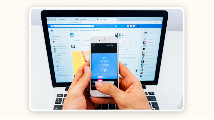 Personne utilisant smartphone devant ordinateur affichant réseau social Facebook ouvert.