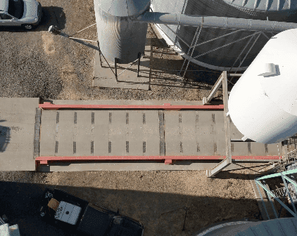 Aerial photograph of a truck loading platform with a cylinder above a conveyor belt, representing bulk transportation.