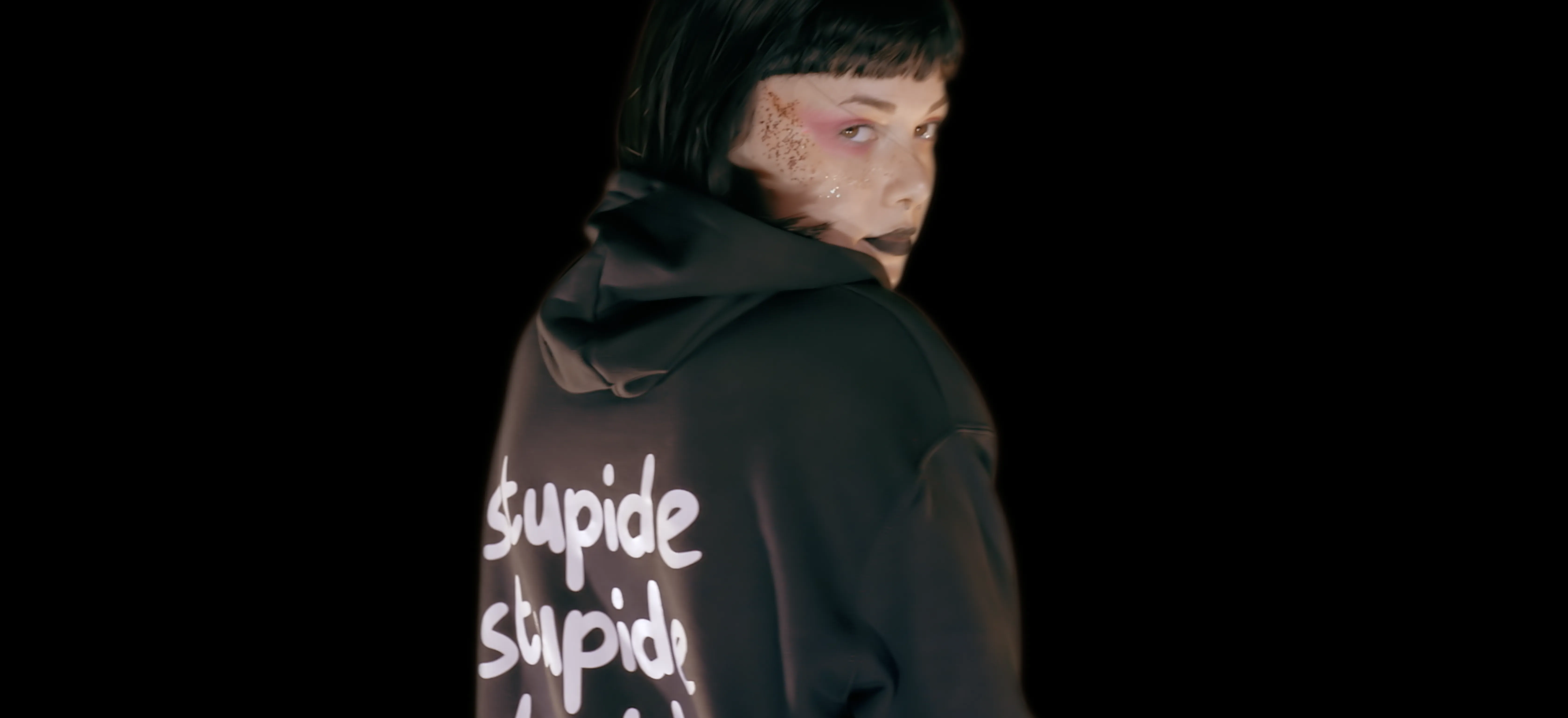 A person wearing a black hoodie with graffiti-style text in white stands against a dark background, adding a bold, edgy contrast to the scene.