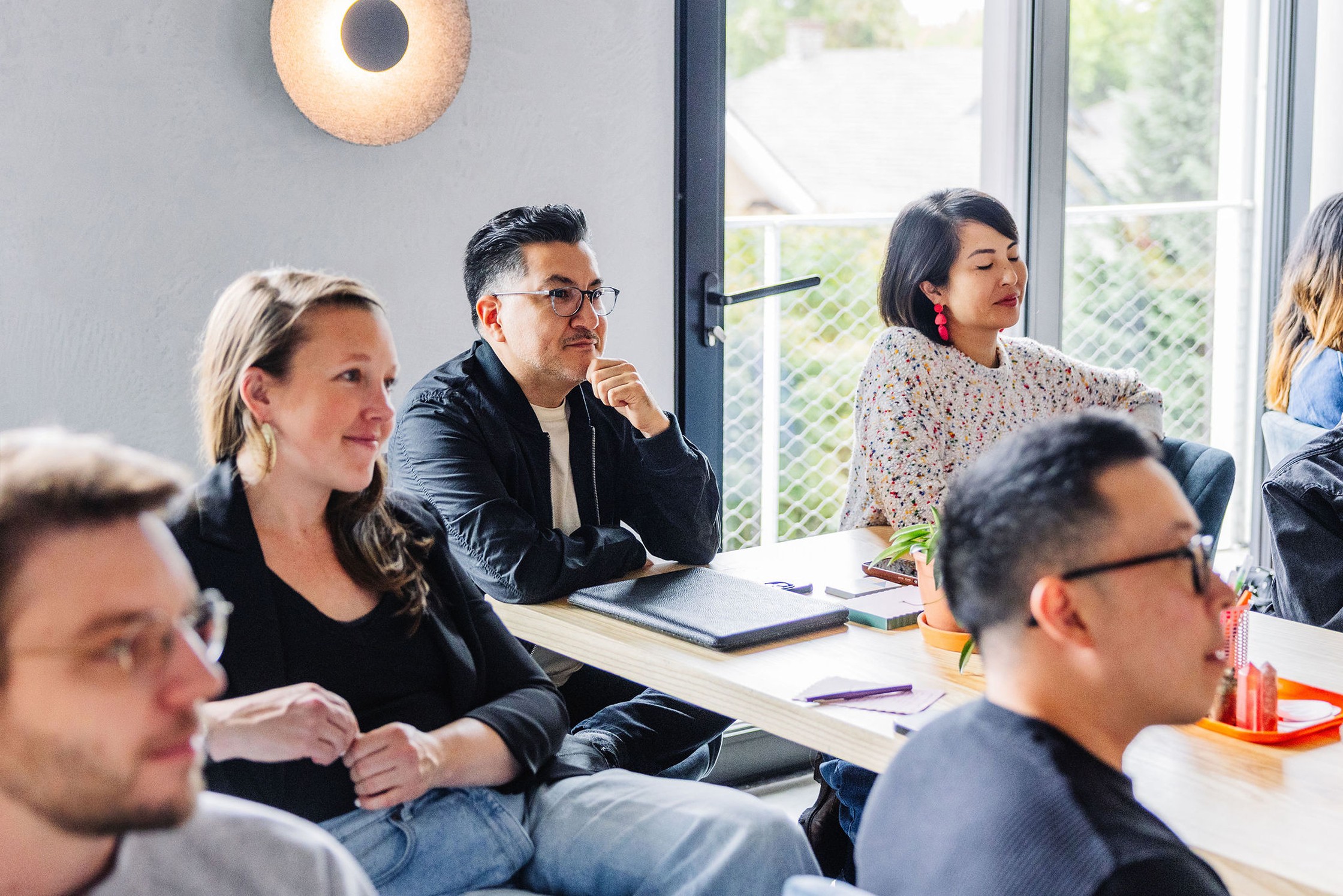 People seated at a table listening attentively during a meeting, with notebooks and pens on the table.