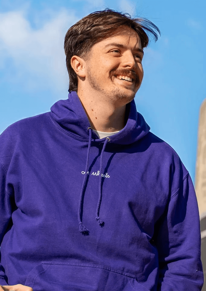 Émile SEGURET, cofondateur de On Wheels, souriant en portant un hoodie violet sous un ciel bleu