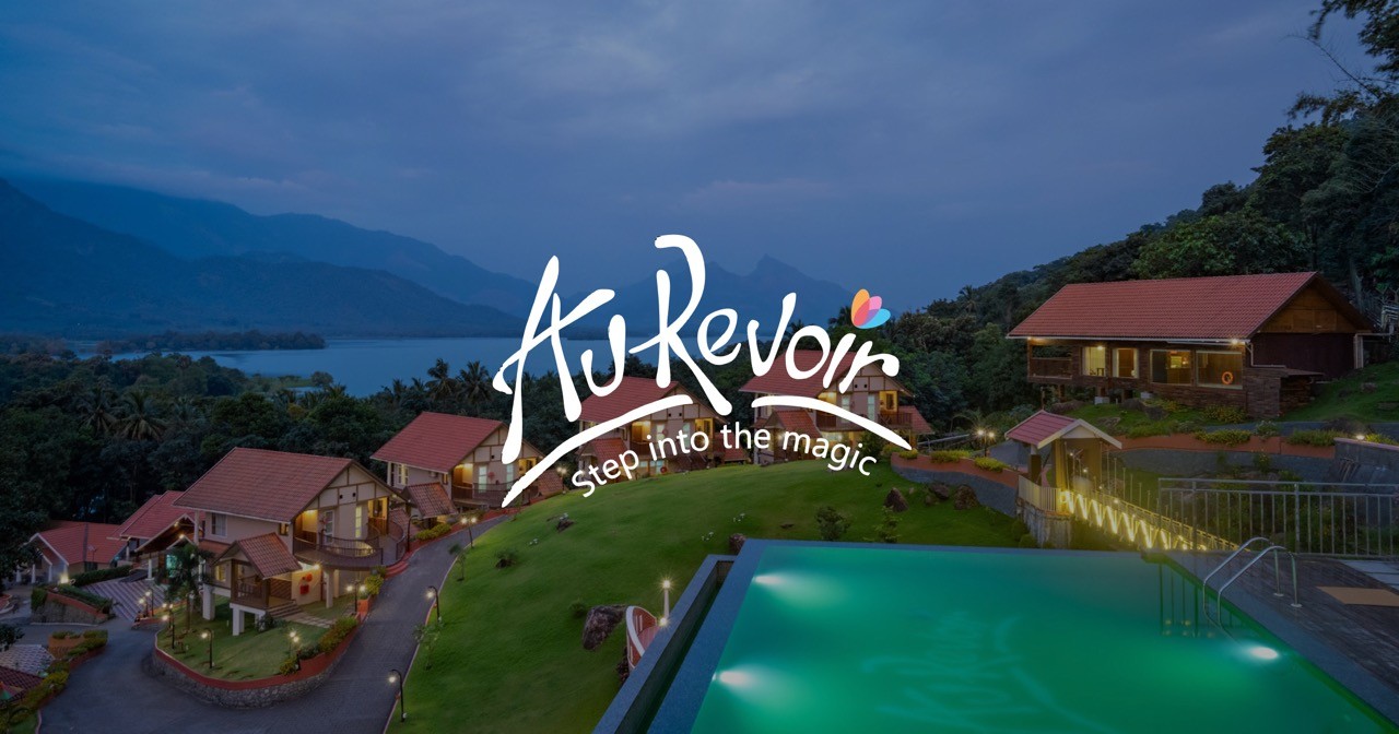 A breathtaking view of Au Revoir Wellness Resort at dusk, nestled in lush greenery with an infinity pool overlooking serene mountains and a lake, offering a tranquil escape into nature and holistic well-being.