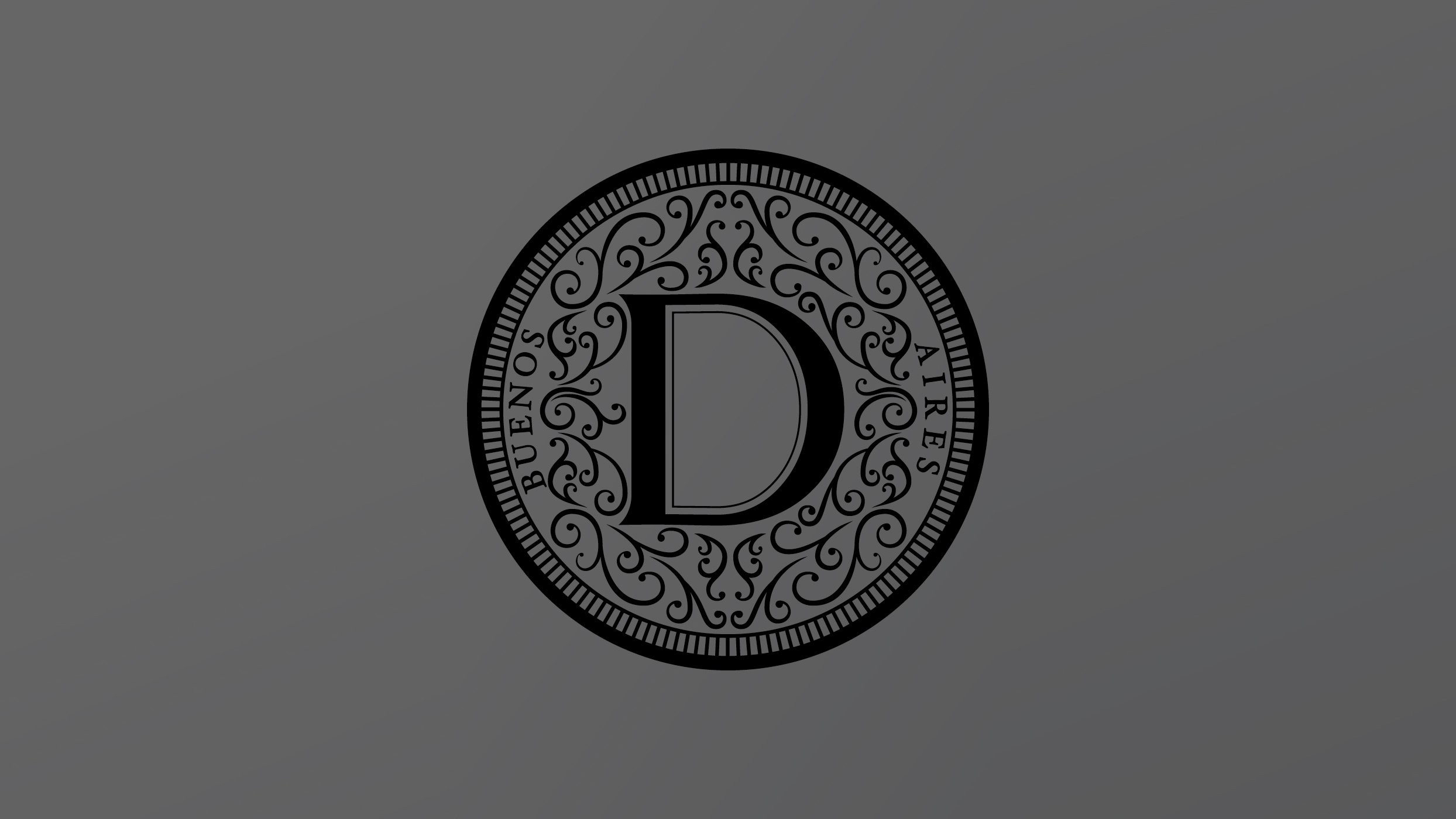 Un emblema circular gris con una gran "D" en el centro, rodeado de patrones florales ornamentados. Las palabras "Buenos Aires" están escritas en el borde interior.