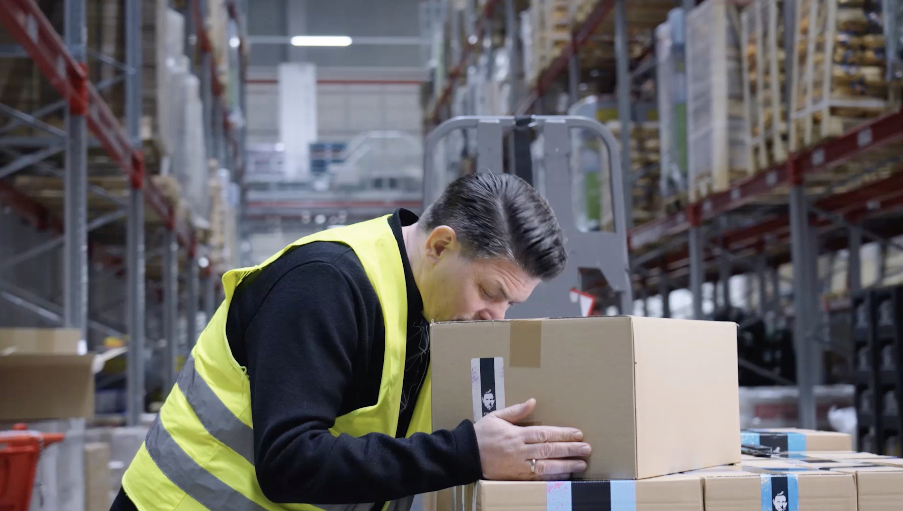 Tim Mälzer inspecting a product package during a branded content production in a logistics warehouse.