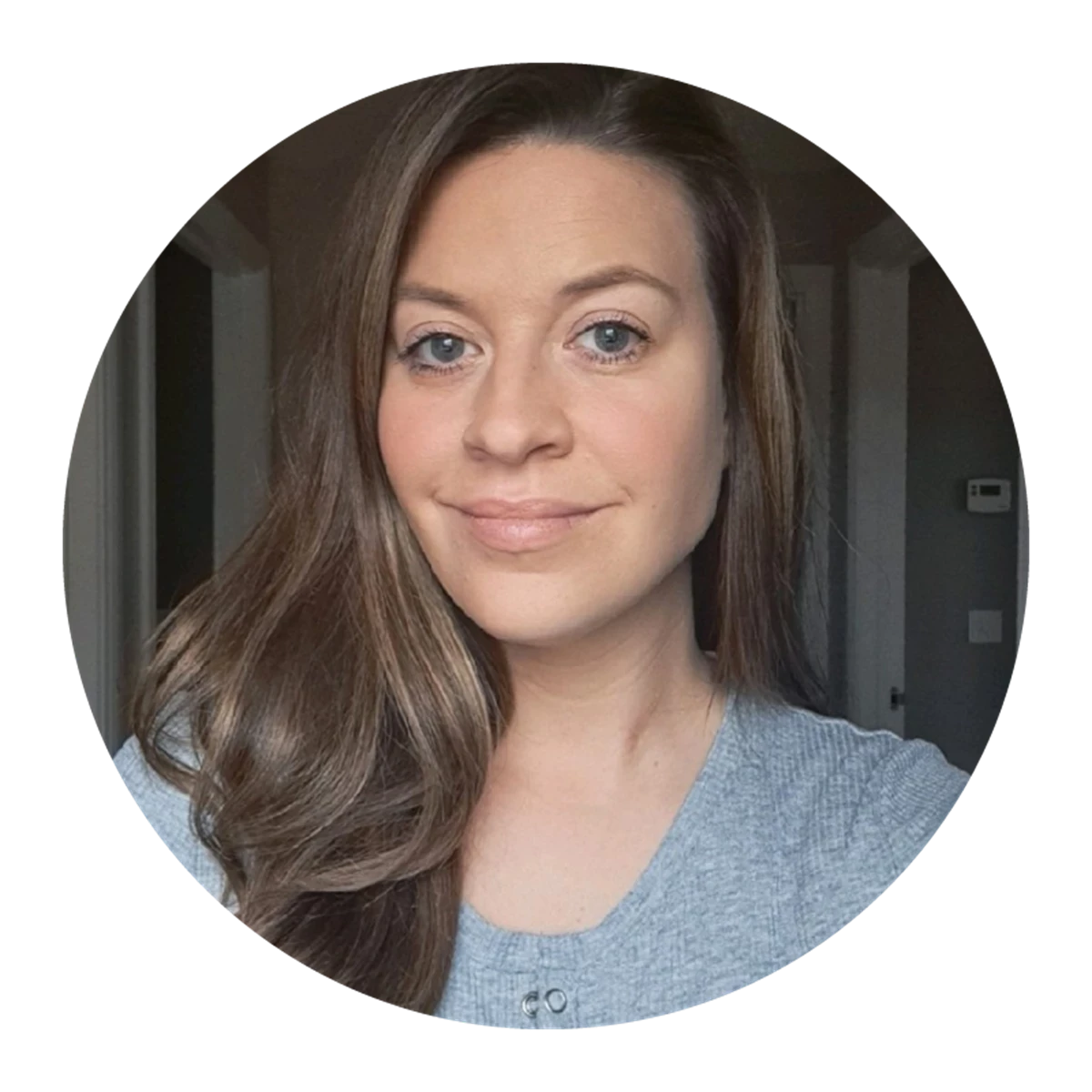 Person with long wavy brown hair wearing a grey top indoors.