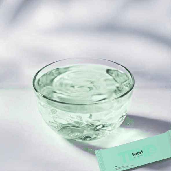 Glass bowl of lightly tinted water with gentle surface movement and a hydration sachet beside it