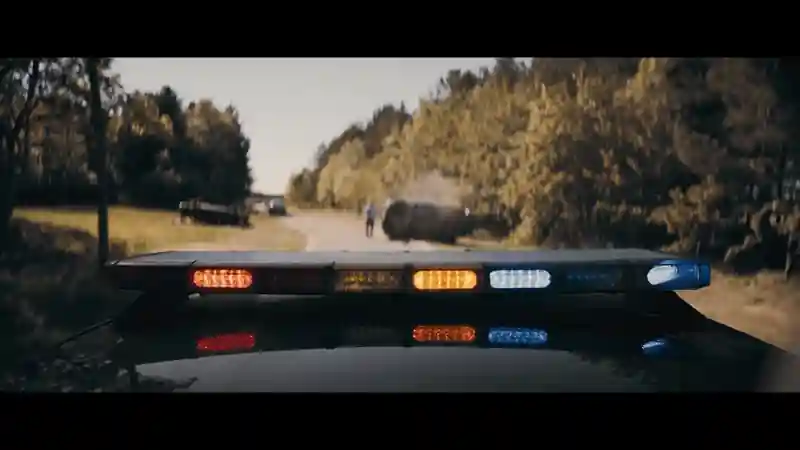 Police vehicle with flashing lights approaching a car accident on a rural road